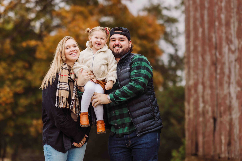 family standing in front of fall colours looking cozy
