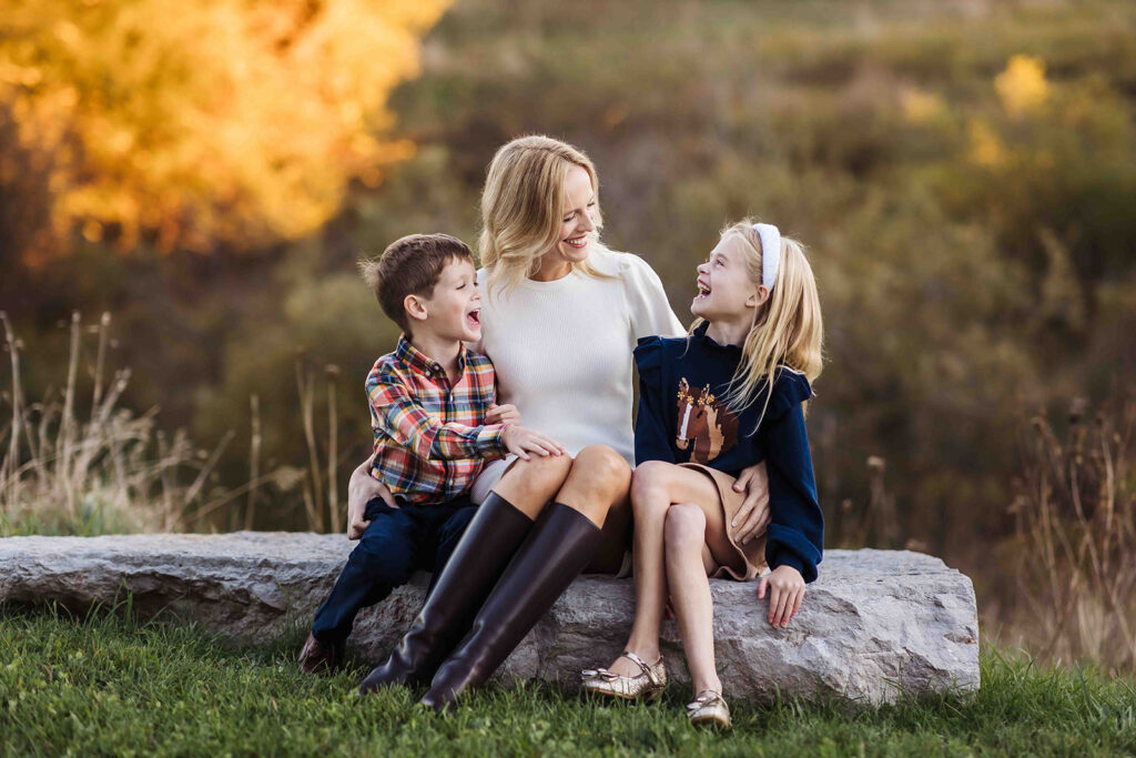 mom and two kids sitting on rock in the fall
