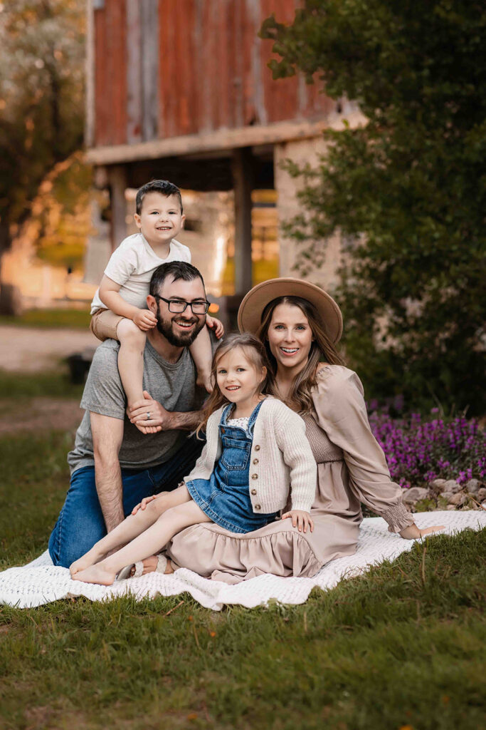 family in neutral fall colours sitting on blanket in front of barn