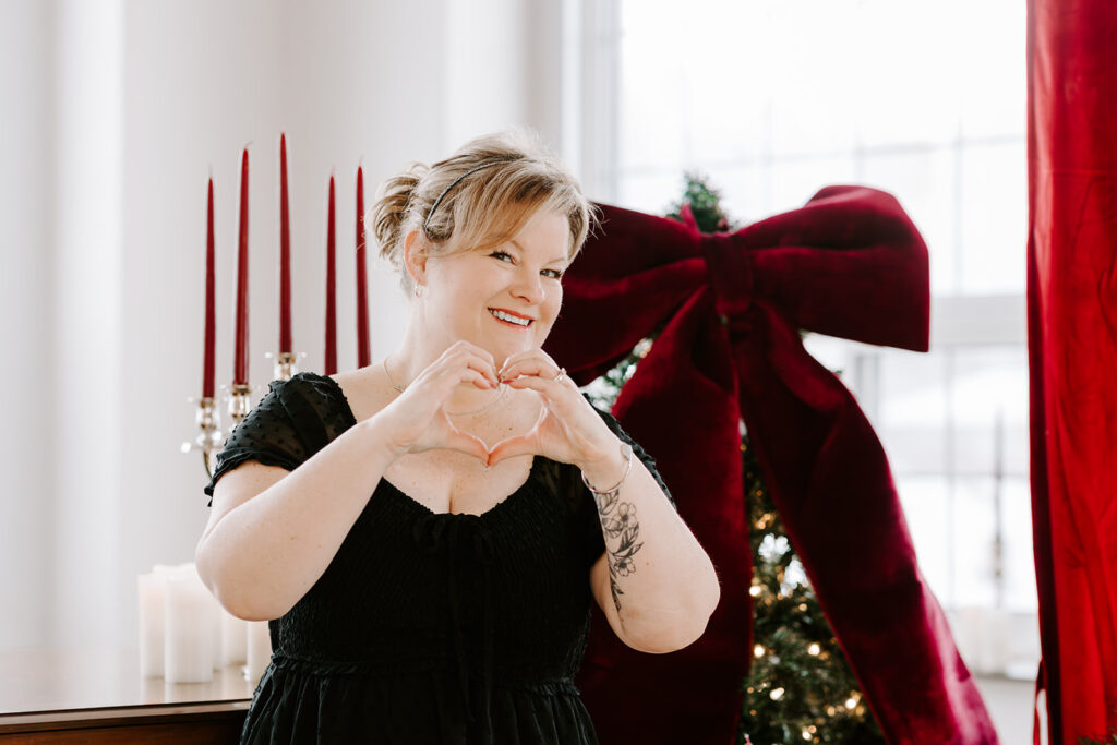 Portrait of Kitchener-Waterloo photographer, Kendra, smiling and forming a heart with her hands during a holiday photoshoot.