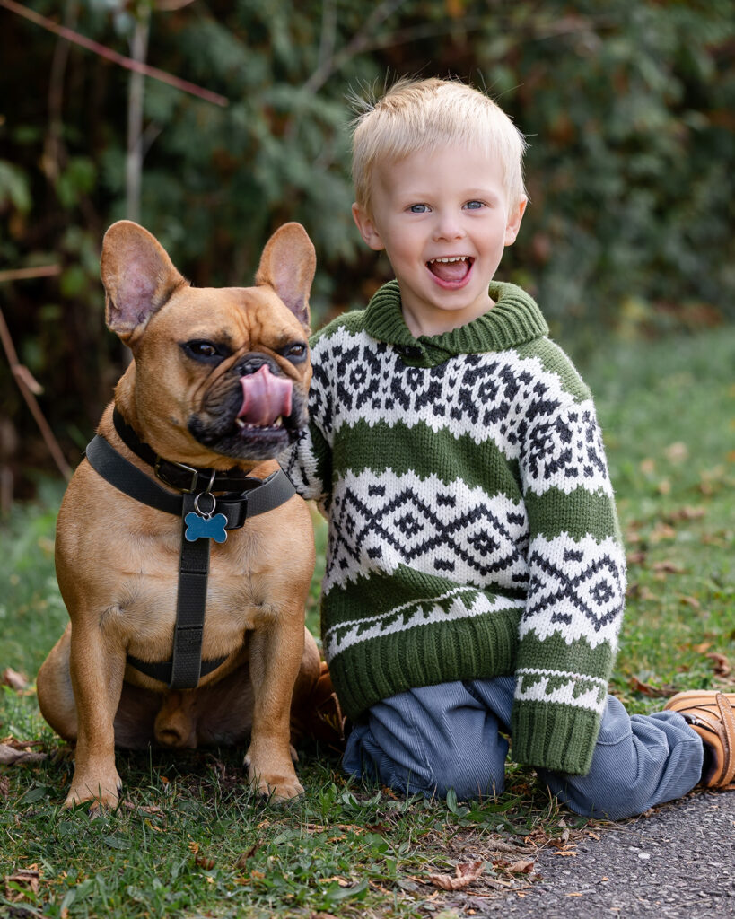 Smiling young child sitting beside a dog during a playful family photography session by Portraits by Kendra, Kitchener-Waterloo photographer.