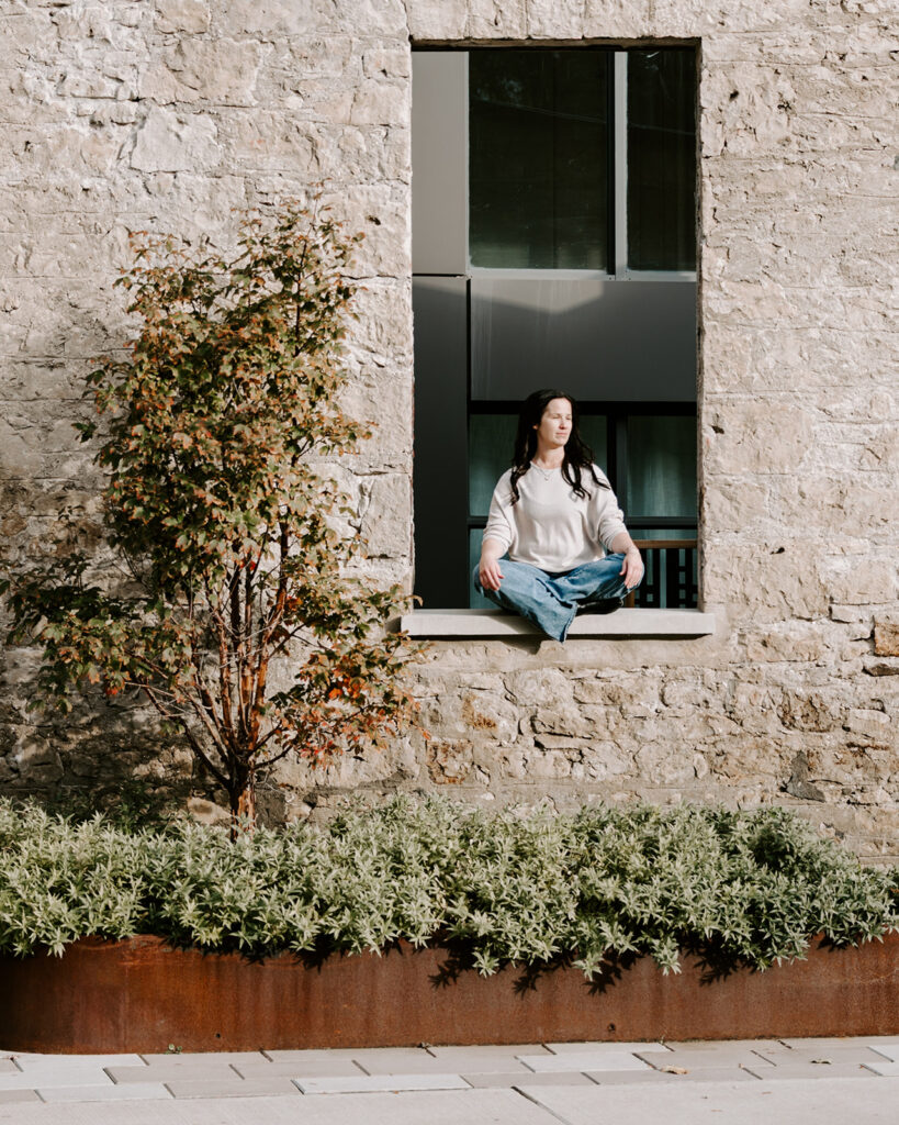 Lifestyle portrait of a woman seated in a stone window opening during a creative branding session in Kitchener-Waterloo. Photographed by Portraits by Kendra.
