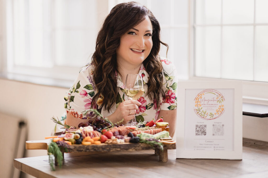 Mary Tchabrazian, owner of Marycuterie, sitting in front of a charcuterie board she made and holding a glass of wine during a branding photoshoot by Portraits by Kendra in Waterloo Region