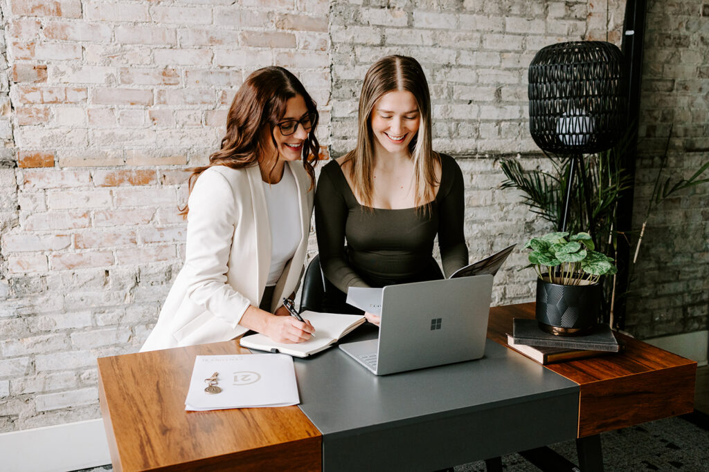 Photo of the The Livingston Team sitting at a desk looking at a computer during a Mother-Daughter Branding Session at West Haus Studio in Downtown Kitchener, taken by Portraits by Kendra