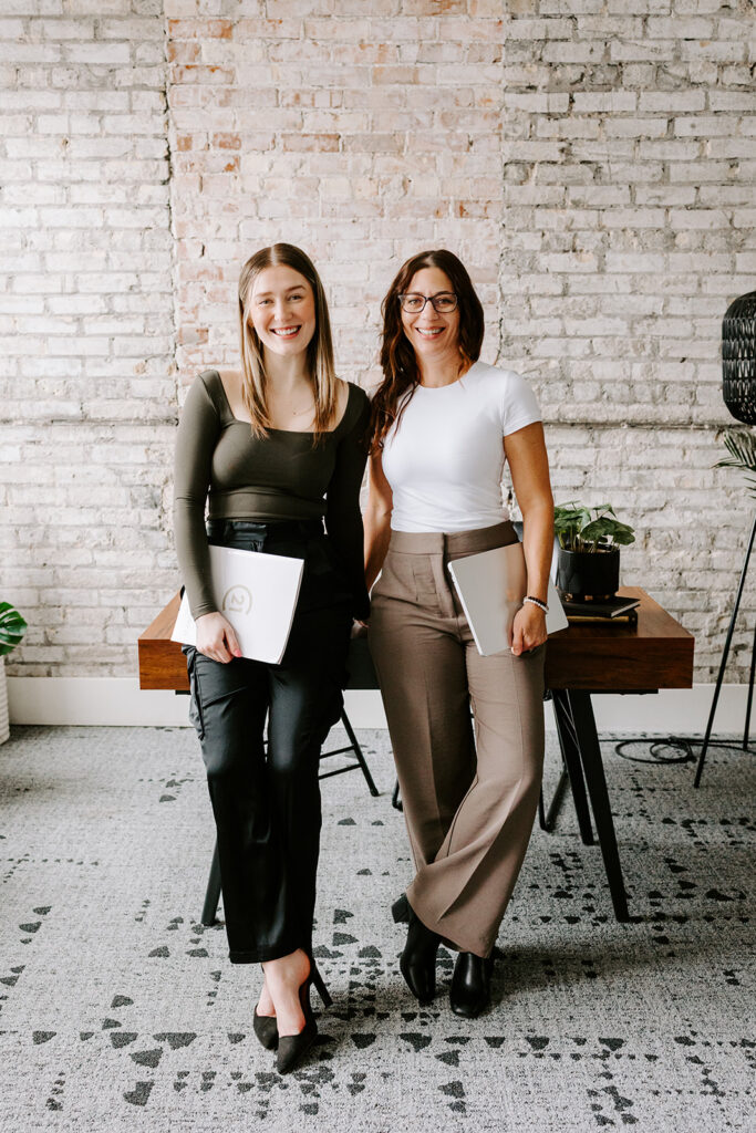 Photo of the The Livingston Team standing in front of a desk during a Mother-Daughter Branding Session at West Haus Studio in Downtown Kitchener, taken by Portraits by Kendra