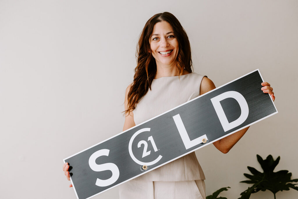 Photo of Isabel Livingston's Mom holding a sold sign during a branding photoshoot in Kitchener, taken by Portraits by Kendra