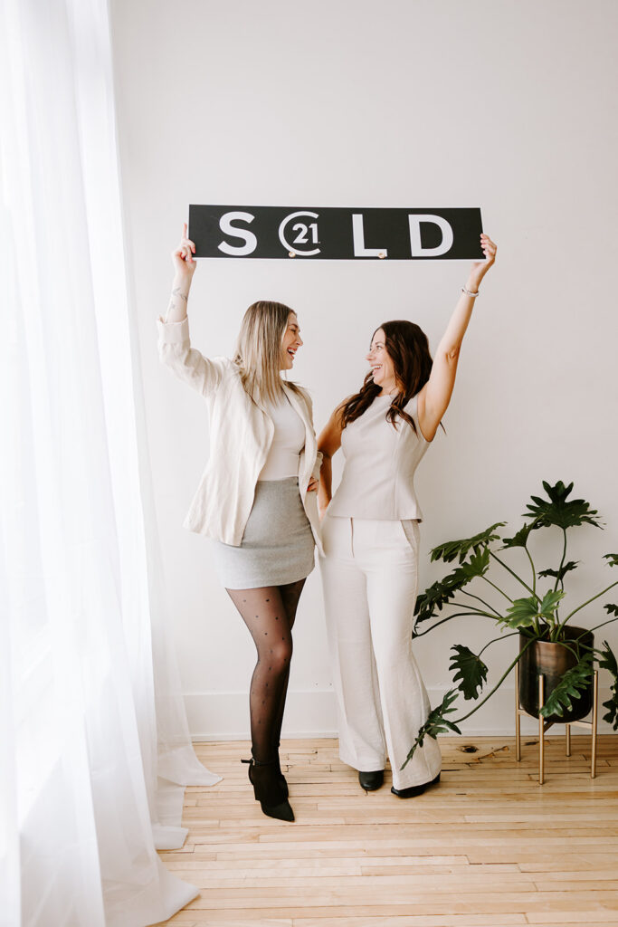 Photo of the The Livingston Team holding a sold sign during a Mother-Daughter Branding Session at West Haus Studio in Downtown Kitchener, taken by Portraits by Kendra