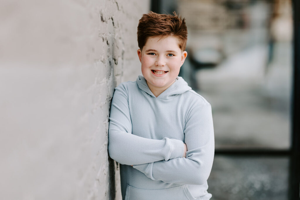 Photo of teen boy with arms crossed leaning against a wall outside in Kitchener-Waterloo.  Photo taken by Portraits by Kendra.