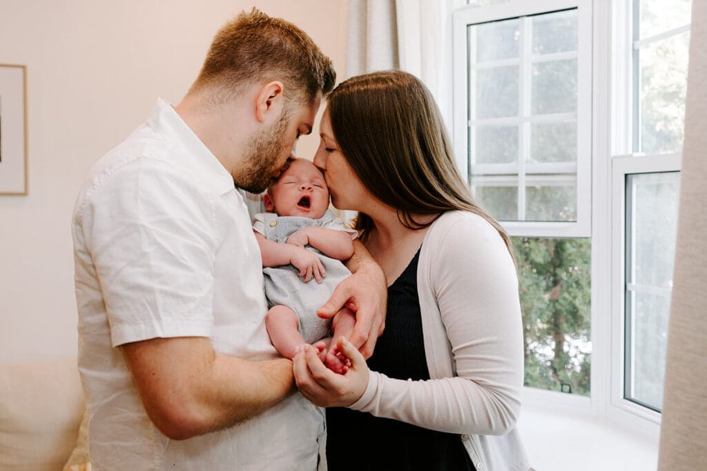 Lifestyle newborn session at home, mom and dad holding baby boy in natural window light, Kitchener-Waterloo family photographer.