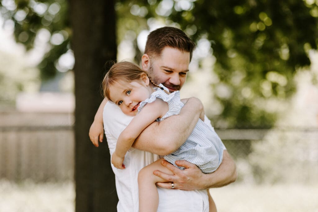 Lifestyle family newborn session outside at home in Kitchener-Waterloo, dad hugging sibling.