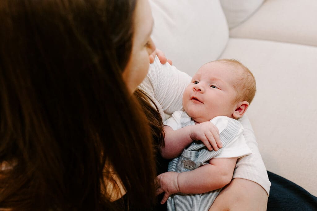 Lifestyle newborn session at home, mom holding baby boy in natural window light, Kitchener-Waterloo family photographer.
