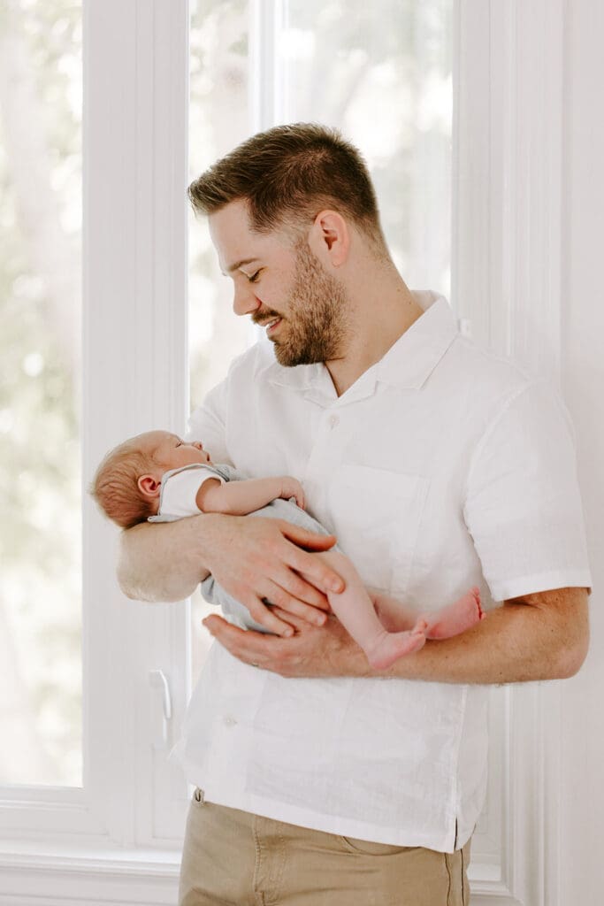 Lifestyle newborn session at home, dad holding baby boy in natural window light, Kitchener-Waterloo family photographer.