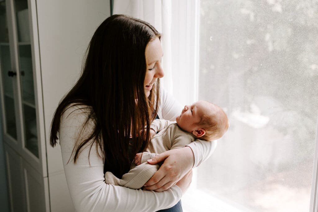 Lifestyle newborn session at home, mom holding baby boy in natural window light, Kitchener-Waterloo family photographer.