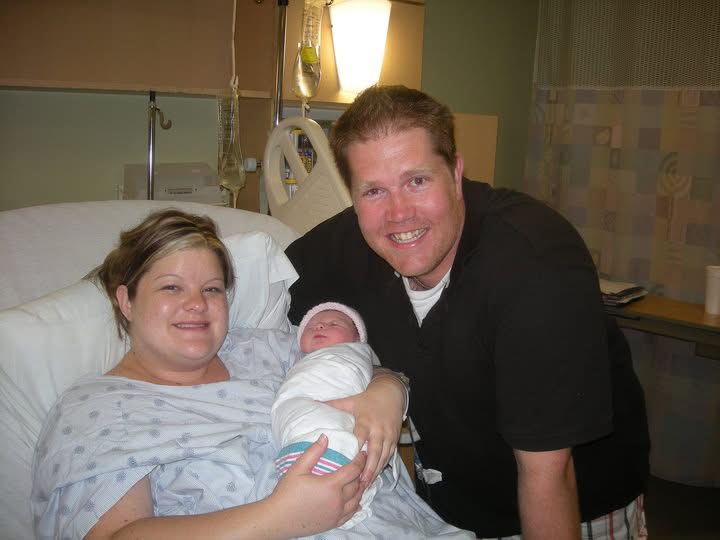 Kendra in her hospital bed holding newborn Chloe with her husband beside them on the day Chloe was born.