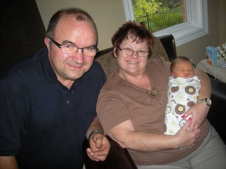 Photo of grandparents holding their newborn granddaughter.