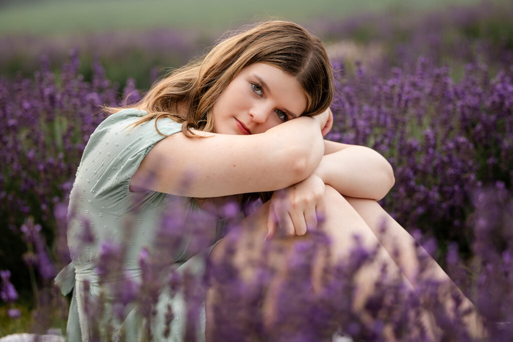 Birthday portrait of teen girl sitting with her arms wrapped around her knees in lavender field in Ayr. 