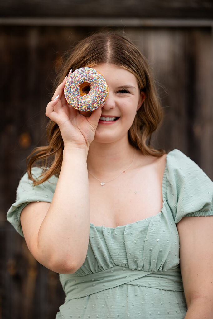 Birthday portrait of teen girl holding a donut,  standing in front of barn doors. 