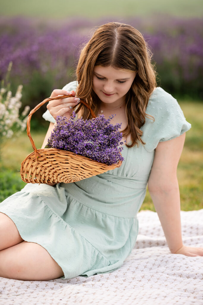 Birthday portrait session of a teen girl admiring lavender in a basket while rsitting on a blanket in a lavender farm in Ayr, Ontario, golden hour natural light photography.
