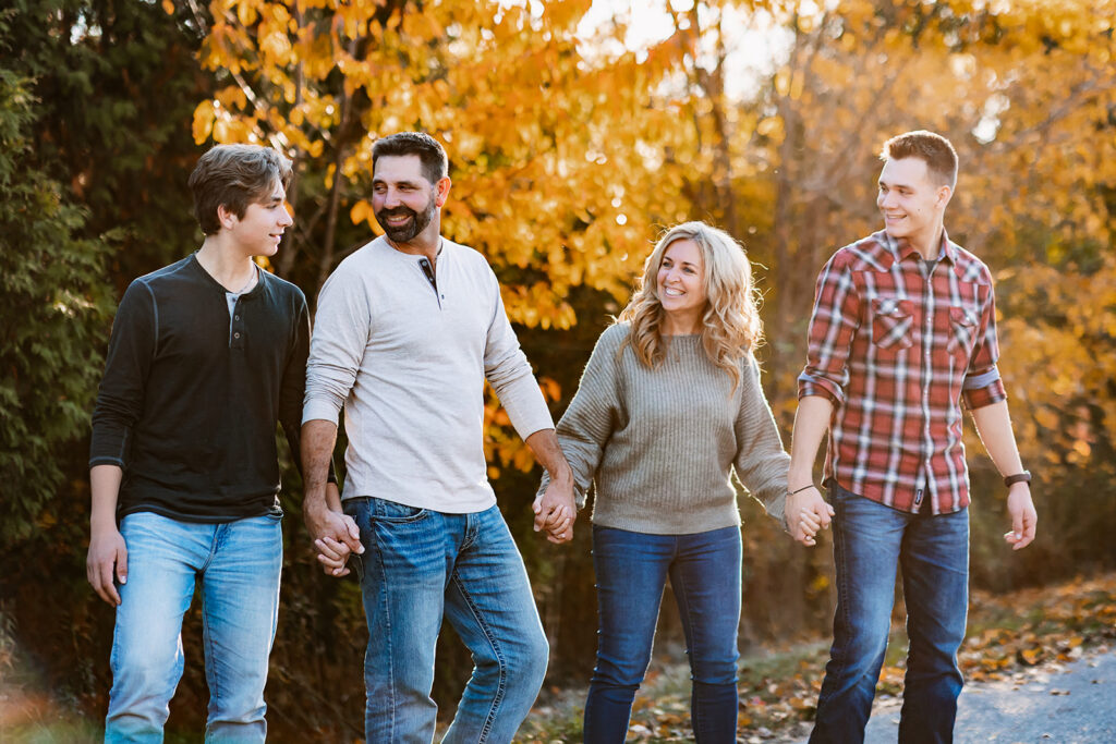 Family of four walking hand in hand beneath colourful autumn trees during a fall family photo session in Kitchener-Waterloo.