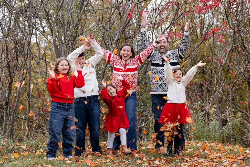 Family of six laughing and tossing autumn leaves during a playful fall family photo session in Kitchener-Waterloo.